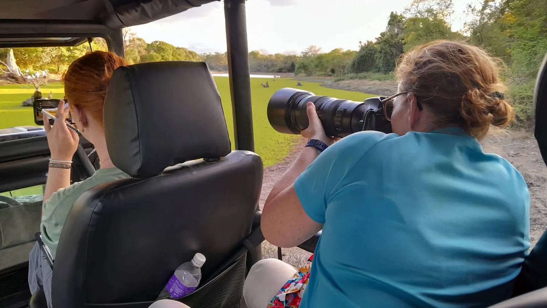 A volunteer photographing wildlife with a long lens from an open jeep beside a lake